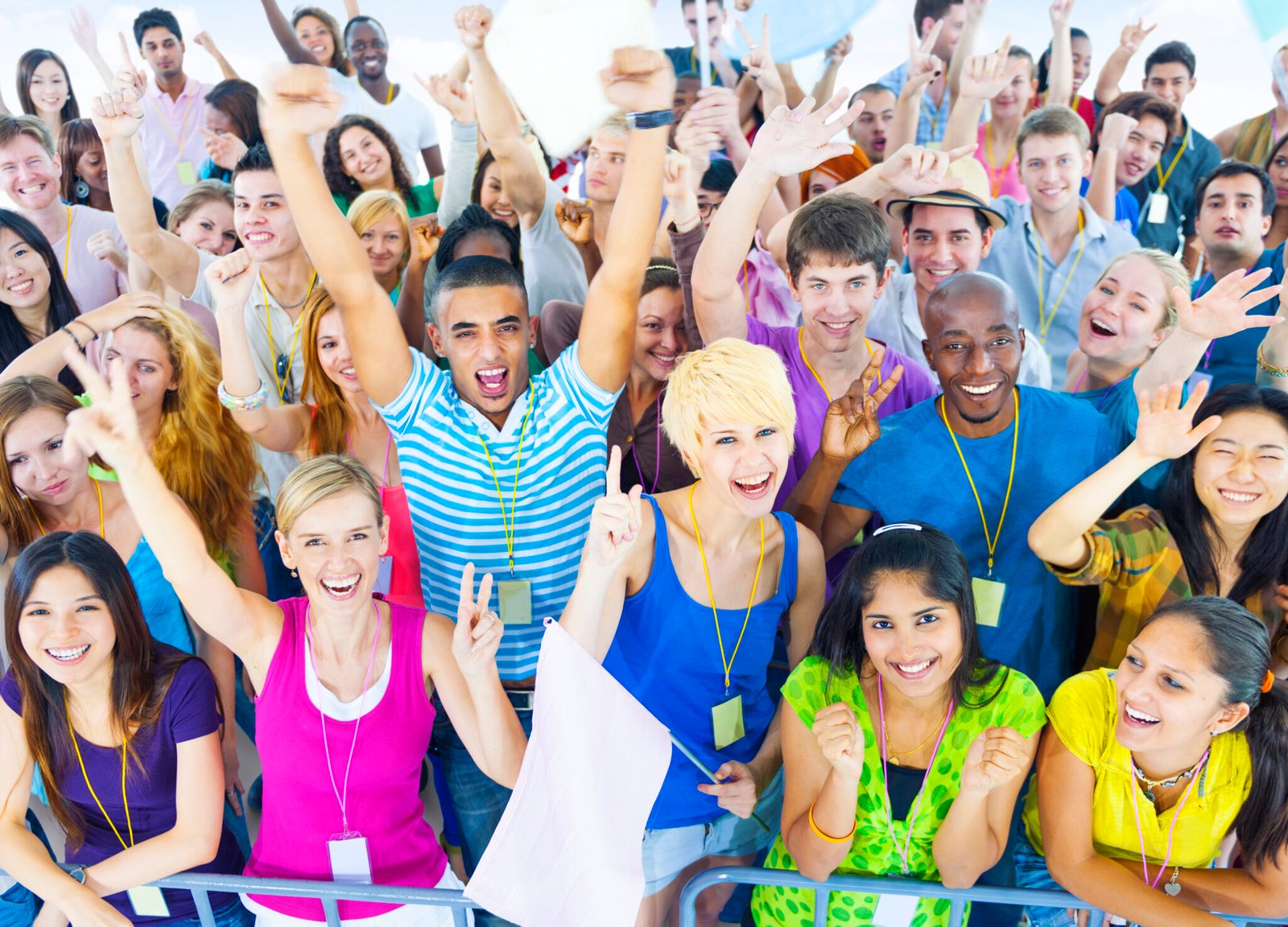 A large, joyful group of workshop participants with lanyards, arms raised in celebration