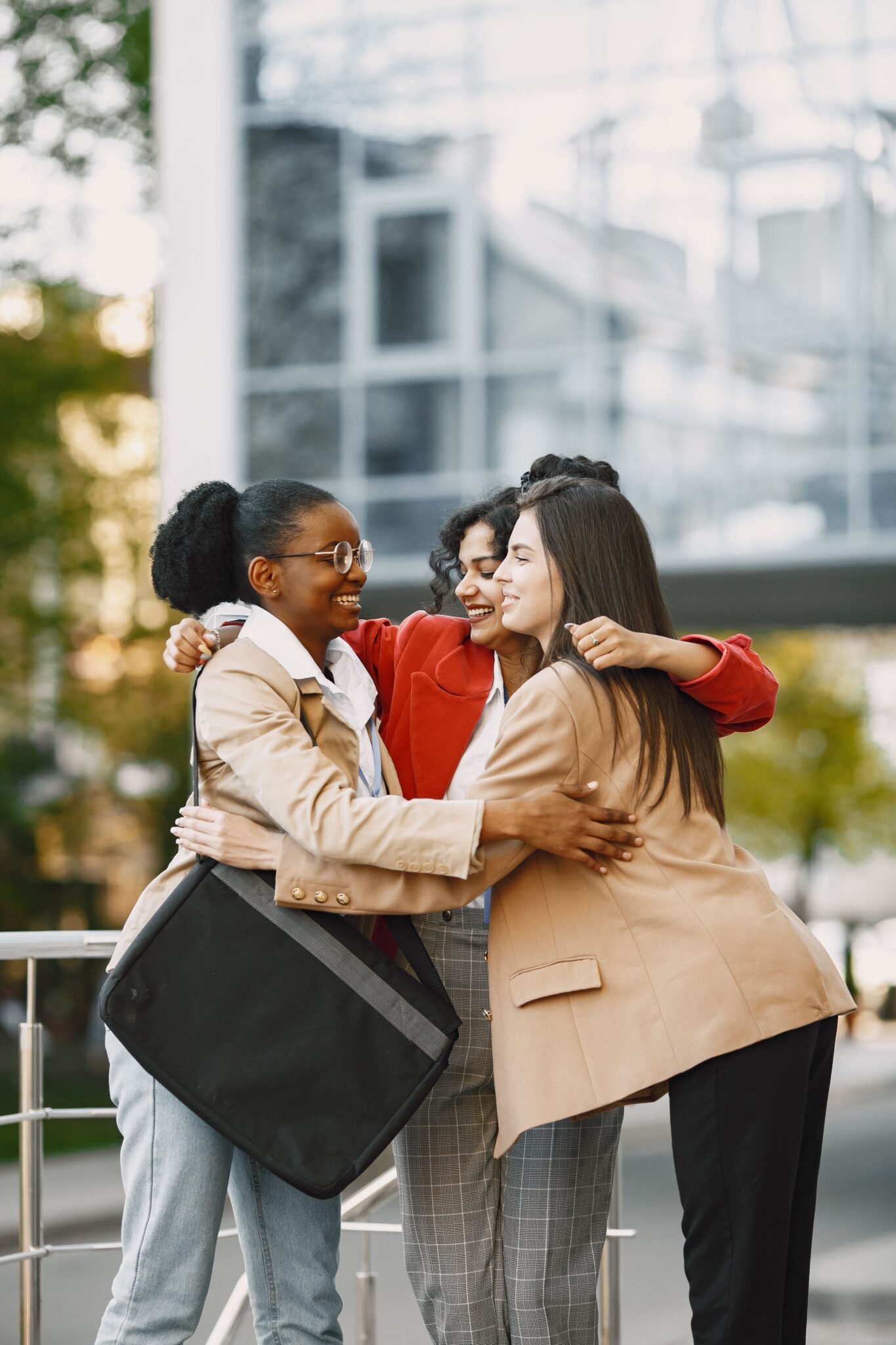 Three women in blazers embracing and smiling together outside