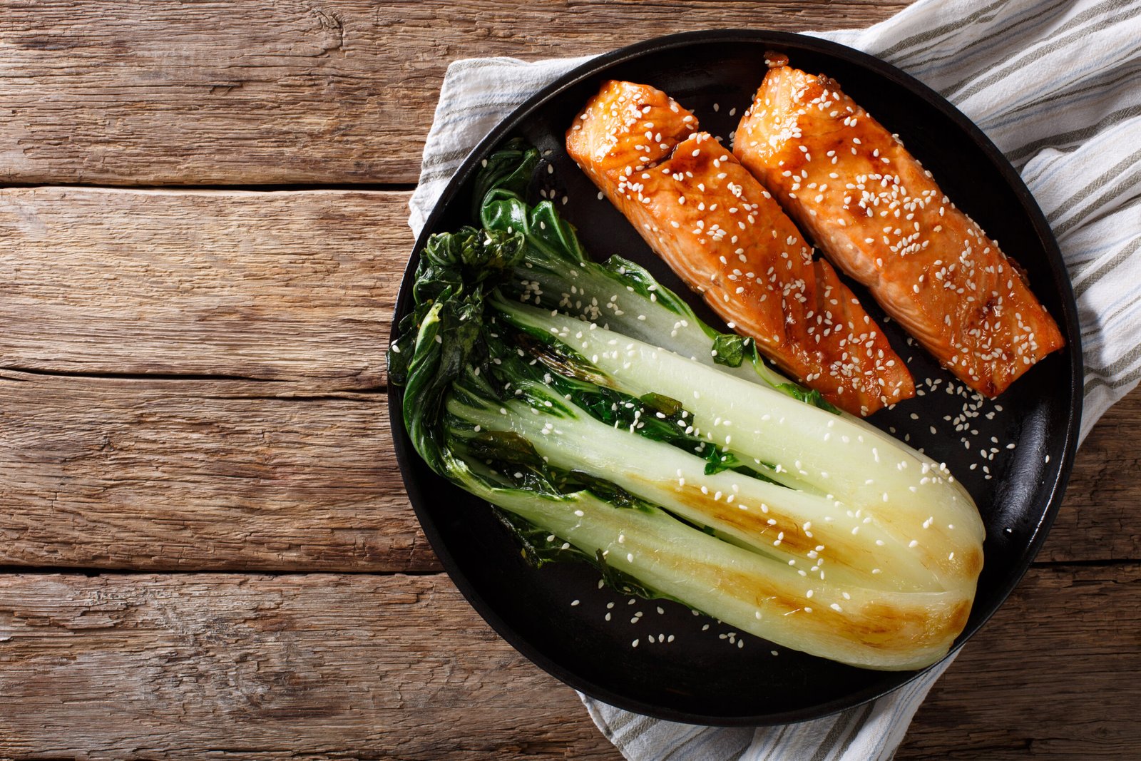 Sesame-glazed salmon fillets with seared bok choy on a black plate